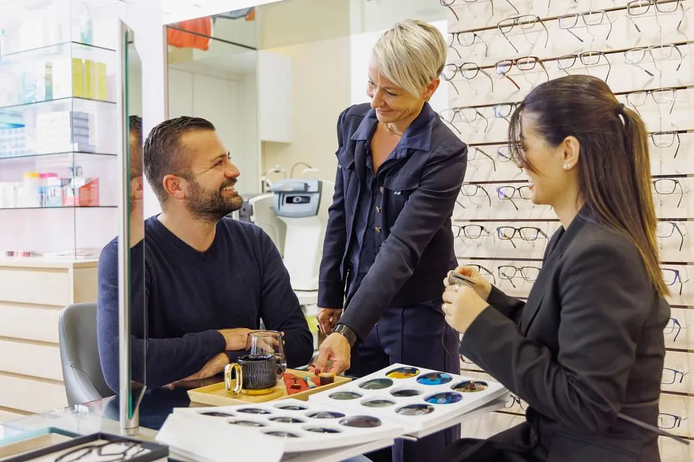Brillenkontrolle, schwarze Frau und Kunde mit Ladenmitarbeiter und Optiker, die auf die Linse schauen. Augenberatung, Beurteilung des Lächelns und der Brille in einem Rahmengeschäft für Sehtest und Verschreibungsprüfung für die Augen
